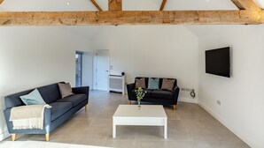 A spacious living area with a high ceiling, exposed wooden beams, a white coffee table, two sofas, and a flat-screen TV mounted on the wall. - Buckley Farm, Barn 1 - UK36588 (Oswestry)