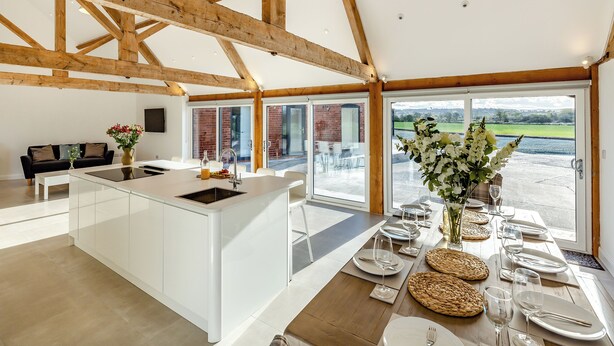 A spacious kitchen with a large island, wooden beams, and a view to the outside. - Buckley Farm, Barn 1 - UK36588 (Oswestry)