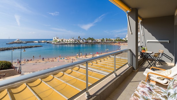 A balcony with yellow sun loungers, a small table with a bottle, and a chair.