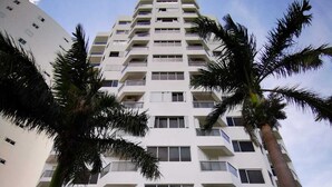 Een hotel met meerdere verdiepingen, een centraal gelegen ingang, palmbomen en een heldere lucht.