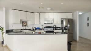 Een moderne keuken met witte kastjes, een centraal eiland, een magnetron, een koelkast en een spoelbak.