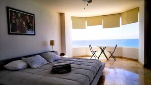Een slaapkamer met een bed, een plafondventilator, een raam met jaloezieën en uitzicht op zee.
