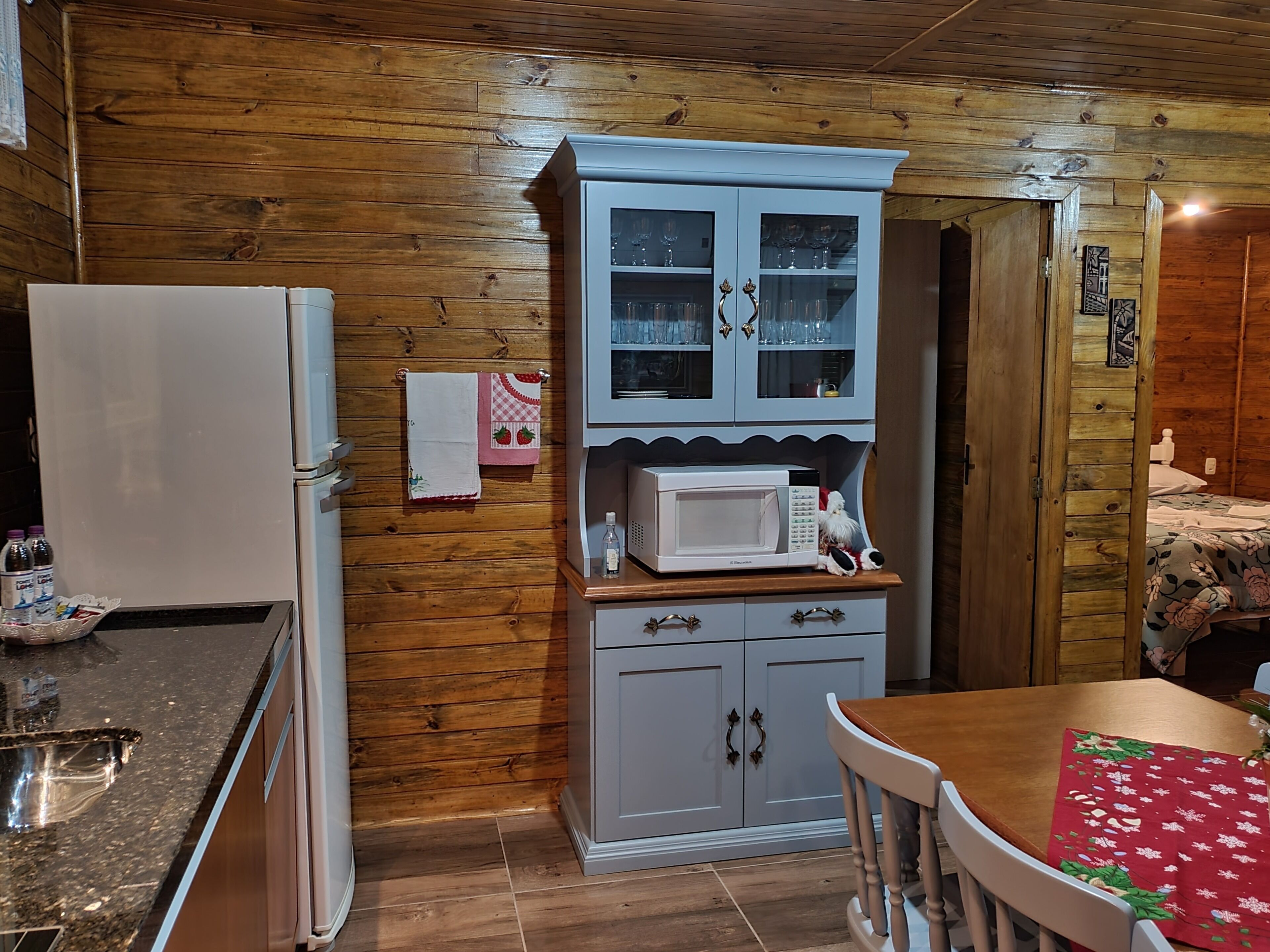 A compact kitchen with wooden walls, a white refrigerator, a microwave, and a small cabinet with glass doors.