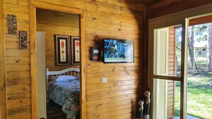 A wooden cabin room with a bed, a television, and a view of the outdoors. - Sitio Recanto Feliz (Gramado)