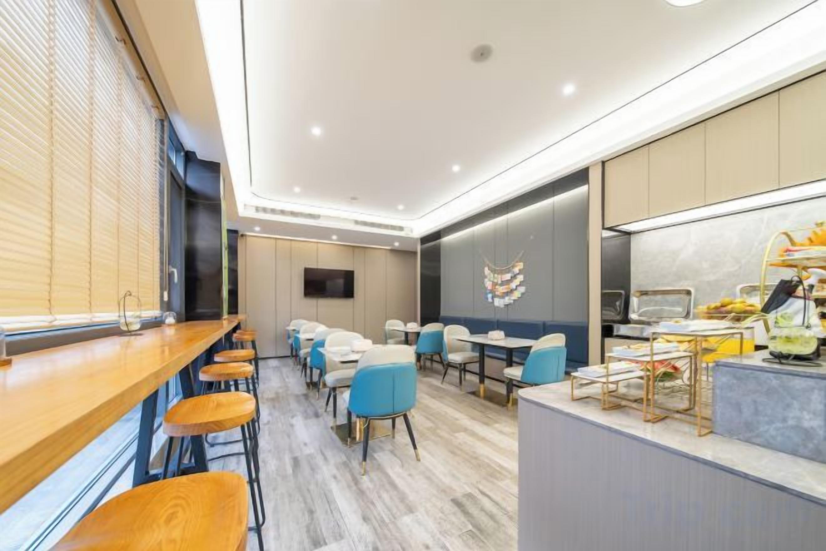 A modern hotel room with a wooden bar, seating area, and a kitchen counter.