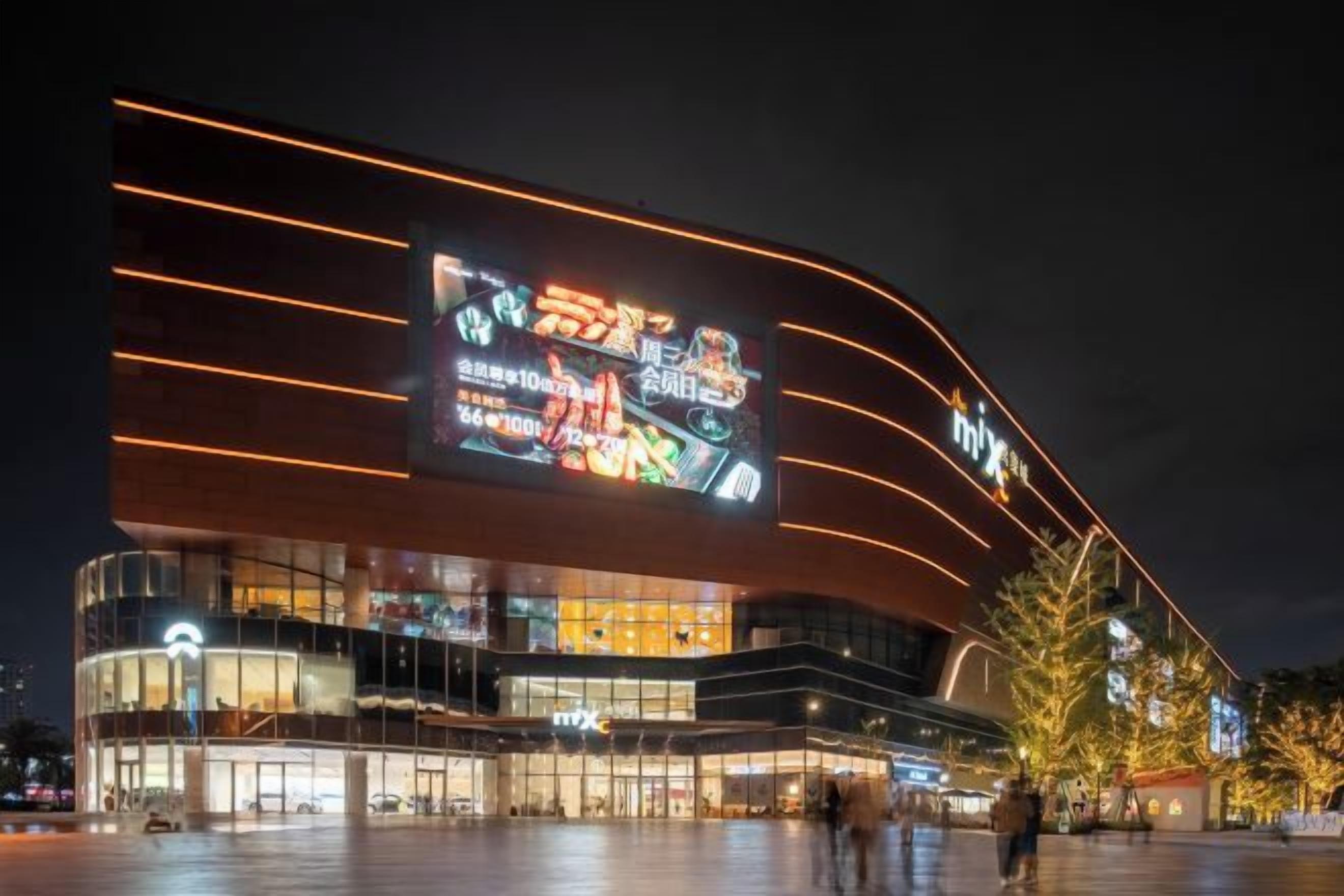 A modern building with a large illuminated sign, glass facade, and a curved design.