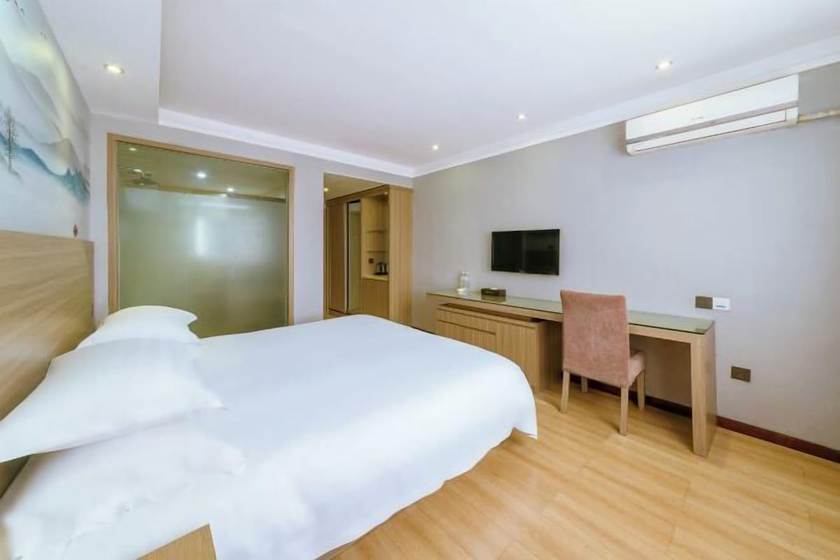 A hotel room with a bed, a desk, a chair, a television, and an air conditioning unit.