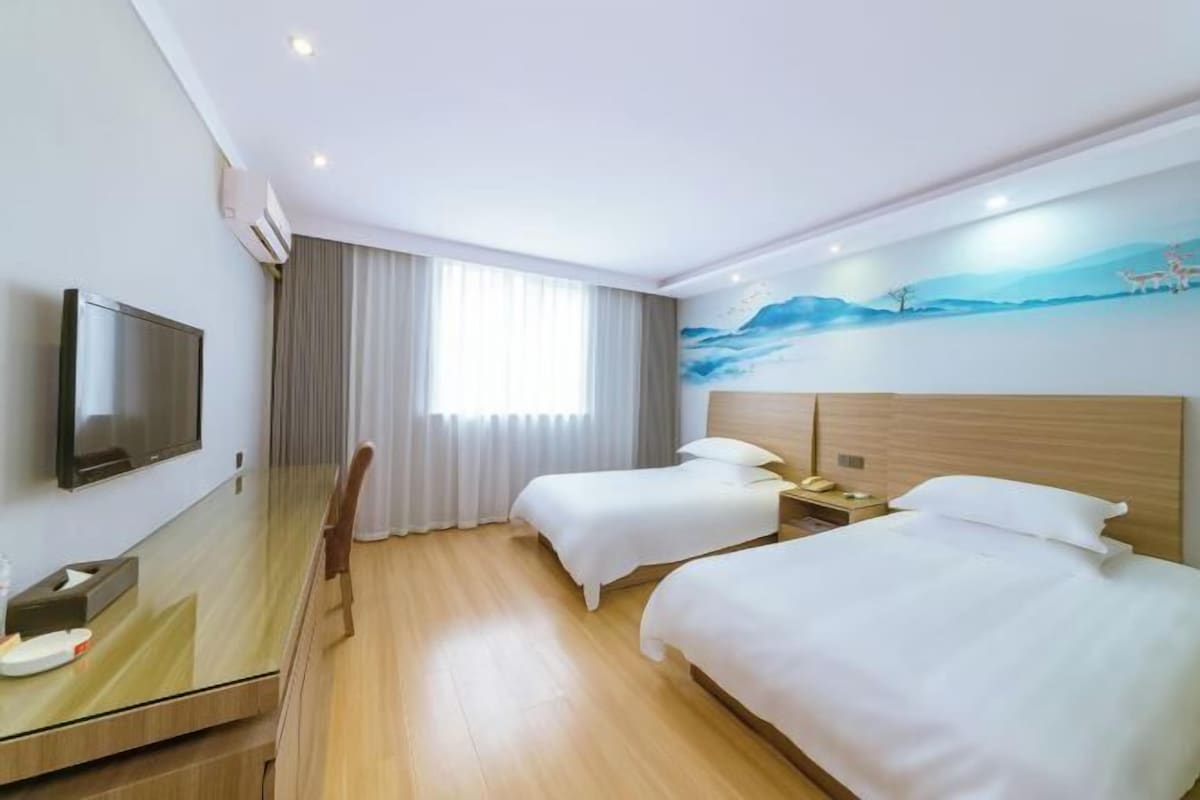 A hotel room with two beds, a flat-screen TV, a desk, and a mural on the wall.