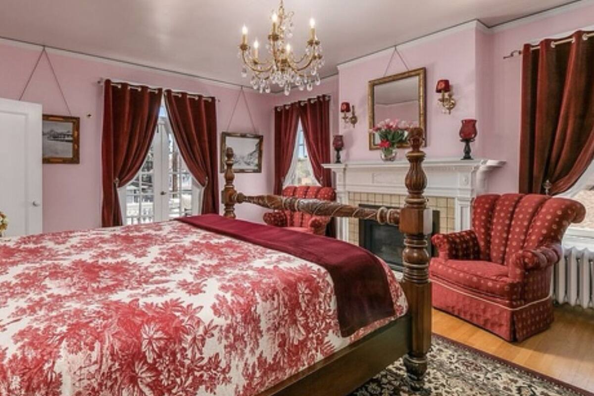 A bedroom with a large bed, a wooden chair, a fireplace, and a chandelier.