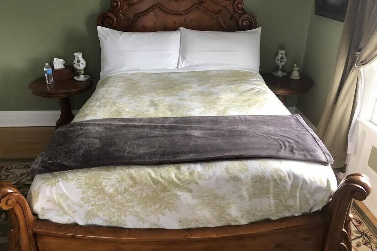 A bed with a floral bedspread, a grey blanket, and a wooden headboard. There are two nightstands with small lamps and a framed picture on the wall.