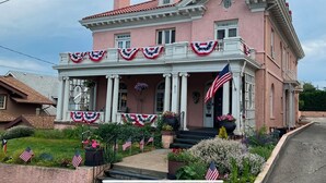 A pink building with a porch decorated with American flags and flowers. - Pendleton House Historic Inn and B&B (Pendleton)