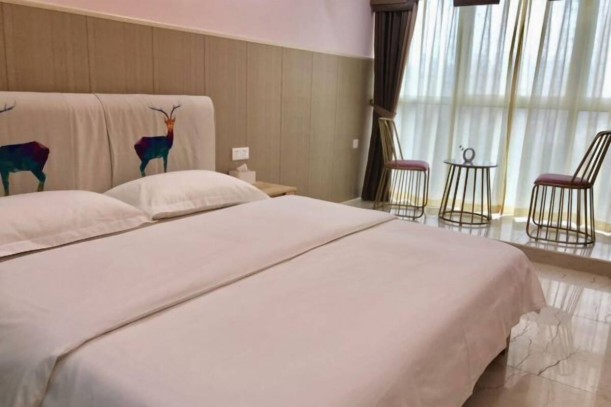 Hotellihuone, jossa on suuri sänky, kaksi tuolia, pieni pöytä ja ikkuna, jossa on verhot.