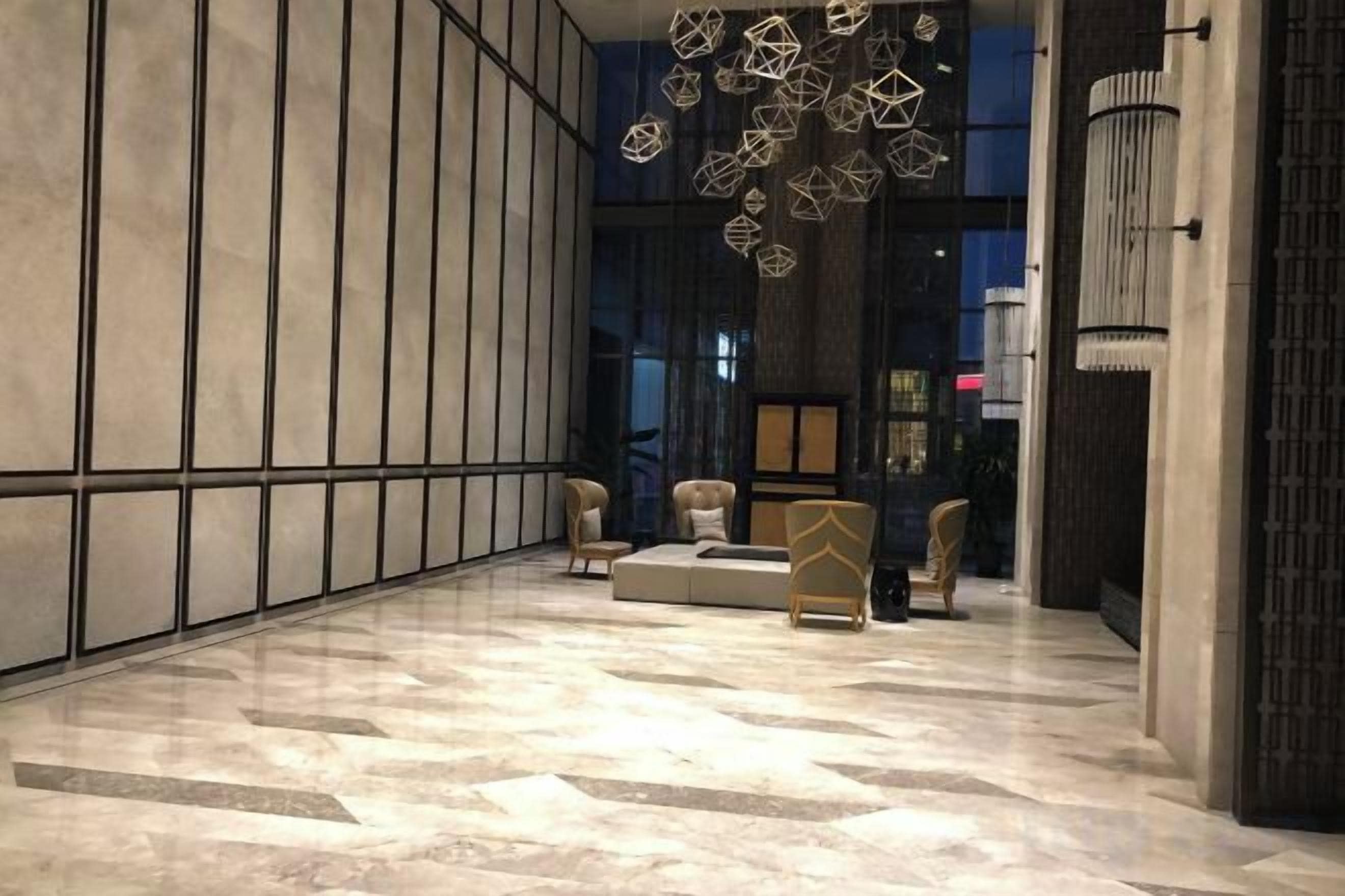 A lobby with a marble floor, seating area, and a modern chandelier.