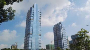 Um edifício alto com fachada de vidro moderna, rodeado por outros edifícios e árvores.