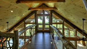 A wooden interior with a high ceiling, wooden beams, and a central staircase leading to a balcony with glass railings. - The VUE Over Blue Ridge - Blue Ridge (Blue Ridge)