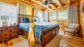 Une chambre dans une cabane en bois, avec un lit, une table de chevet, une chaise et un ventilateur de plafond.