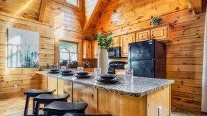 Une cuisine rustique, située dans une cabane en bois, avec un îlot en granit, des tabourets de bar et un réfrigérateur.