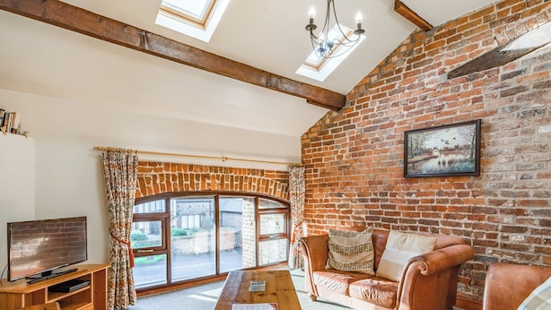 Ein gemütliches Wohnzimmer mit Backsteinwand, Couchtisch aus Holz, Ledersofa und Fernseher auf Holzfuß.