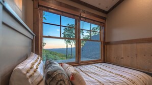 Een slaapkamer met een groot raam, een bed met gestreepte beddengoed en uitzicht op een landschap.