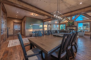 Ein geräumiger Essbereich mit einem großen Holztisch und Stühlen, eine Küche mit Holdelementen und ein Kamin aus Stein.