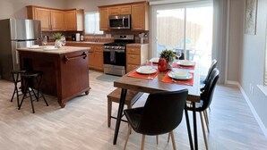 A modern kitchen with wooden cabinets, stainless steel appliances, and a dining area with a table set for two. - Multi Family Home 2 min walk to beach, Sleeps 13 (Oceano)