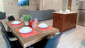 A dining area with a wooden table set for four, surrounded by chairs. A grey sofa and a cabinet with a plant on top are in the background. - Multi Family Home 2 min walk to beach, Sleeps 13 (Oceano)