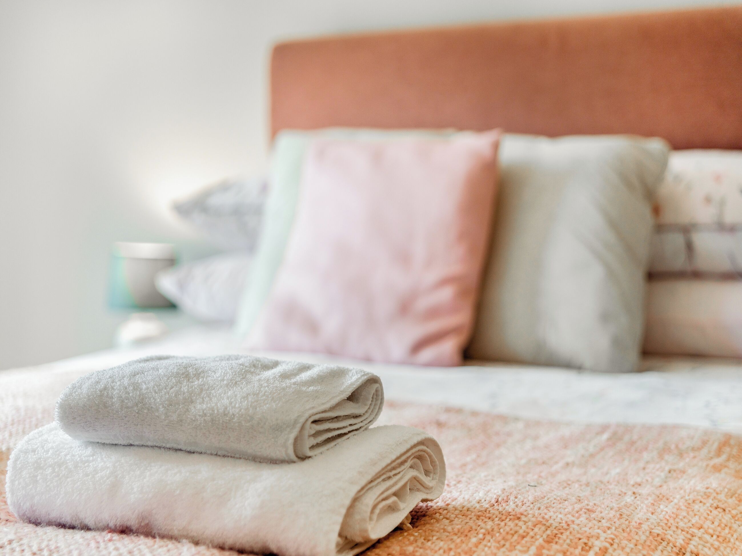 A neatly made bed with rolled towels and a pink textured blanket.
