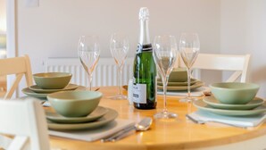 Ein Esstisch ist gedeckt mit grünen Schüsseln, Weingläsern und einer Champagnerflasche.
