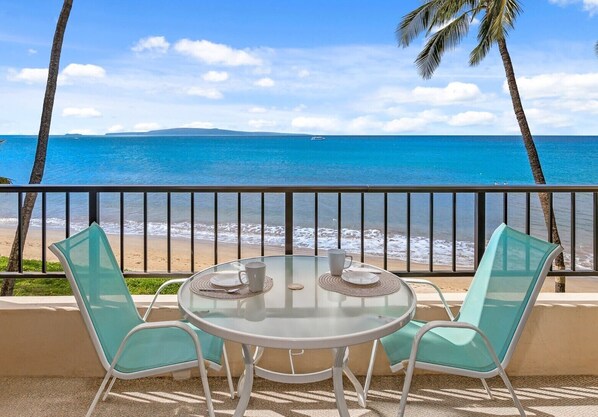 Mesa redonda de vidrio con dos sillas, vista a la playa y palmeras.