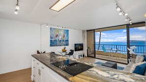 Una cocina moderna con una isla grande, una zona de comedor con vista al mar y un balcón con mobiliario exterior.