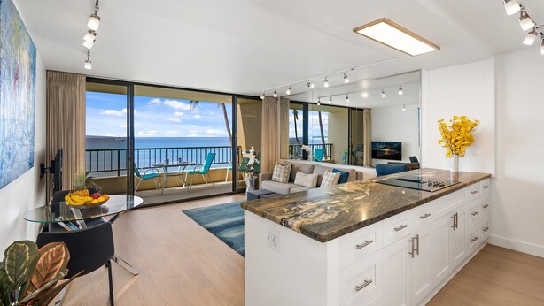 Una sala de estar moderna con un amplio ventanal que da a un balcón, una isla de cocina y un comedor con mesa y sillas.