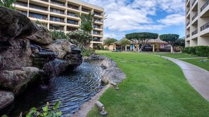 Un patio de hotel con una pequeña cascada, césped bien cuidado y un edificio de varios pisos con balcones.