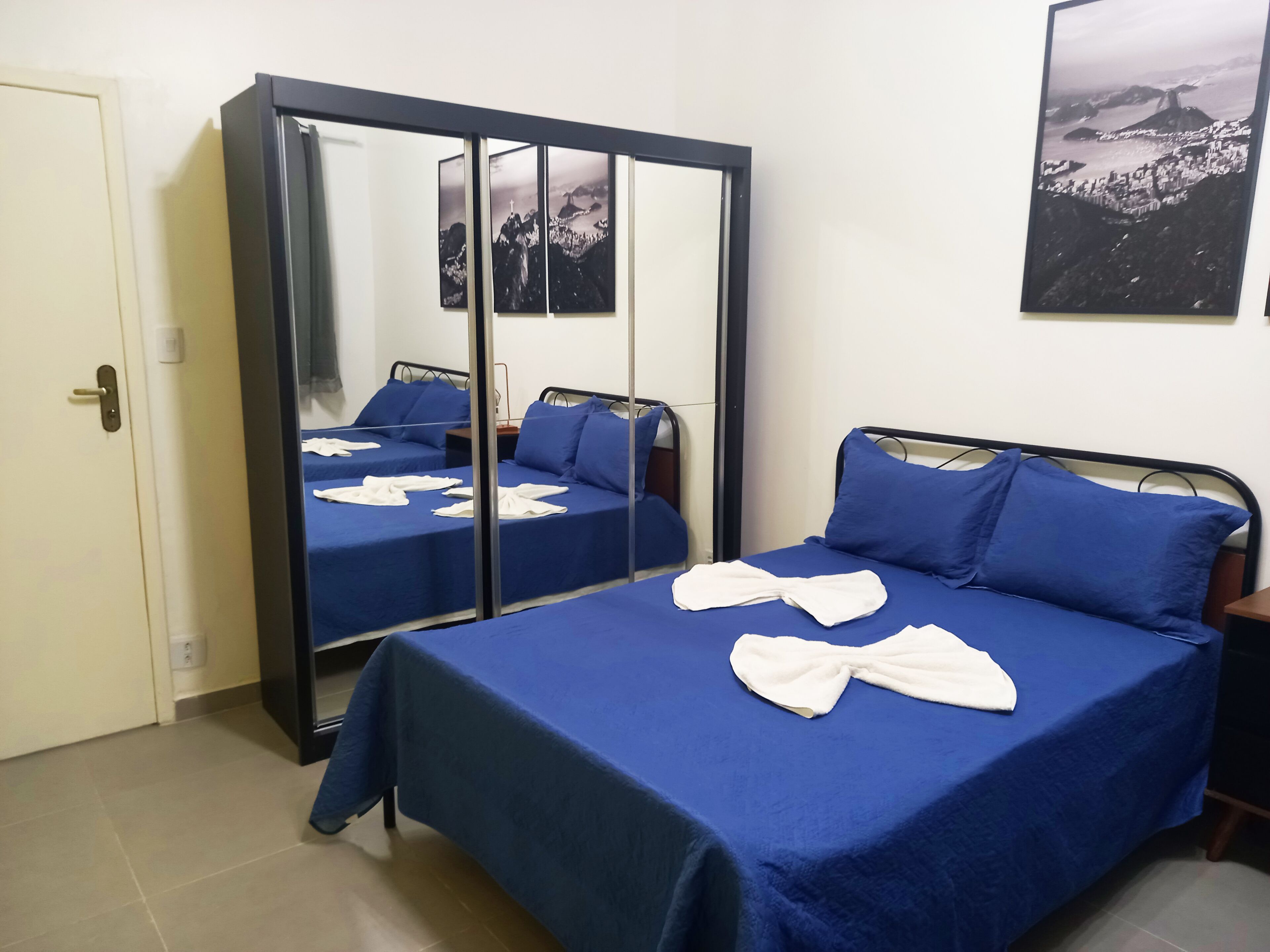 A hotel room with two beds, each with blue bedding and white towels. There is a large mirror on one wall and a framed picture above the beds.