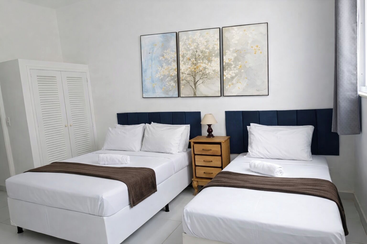 A hotel room with two beds, a nightstand, and a set of white lockers.