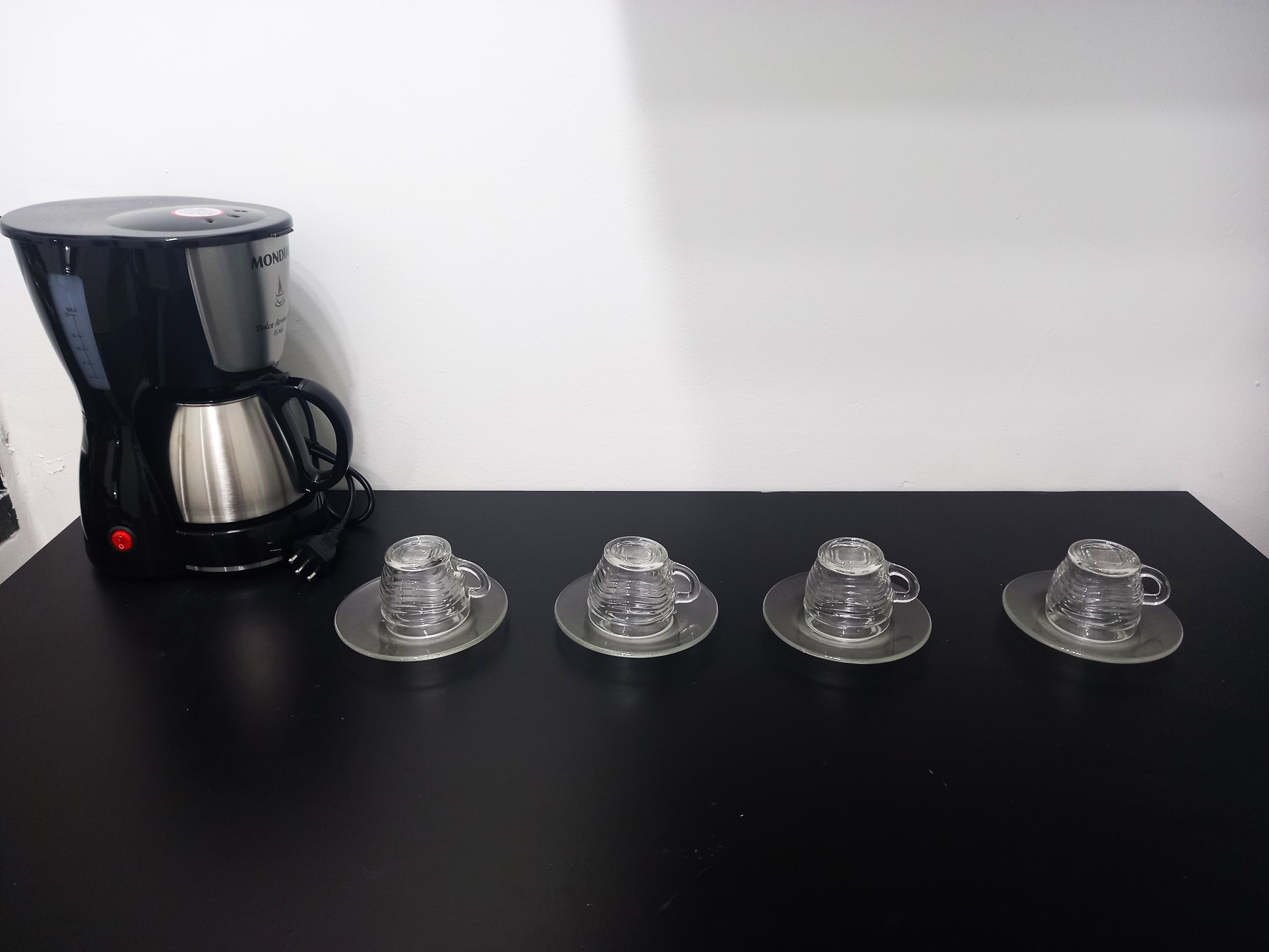 A black coffee maker on a black table with four clear glass cups on saucers.