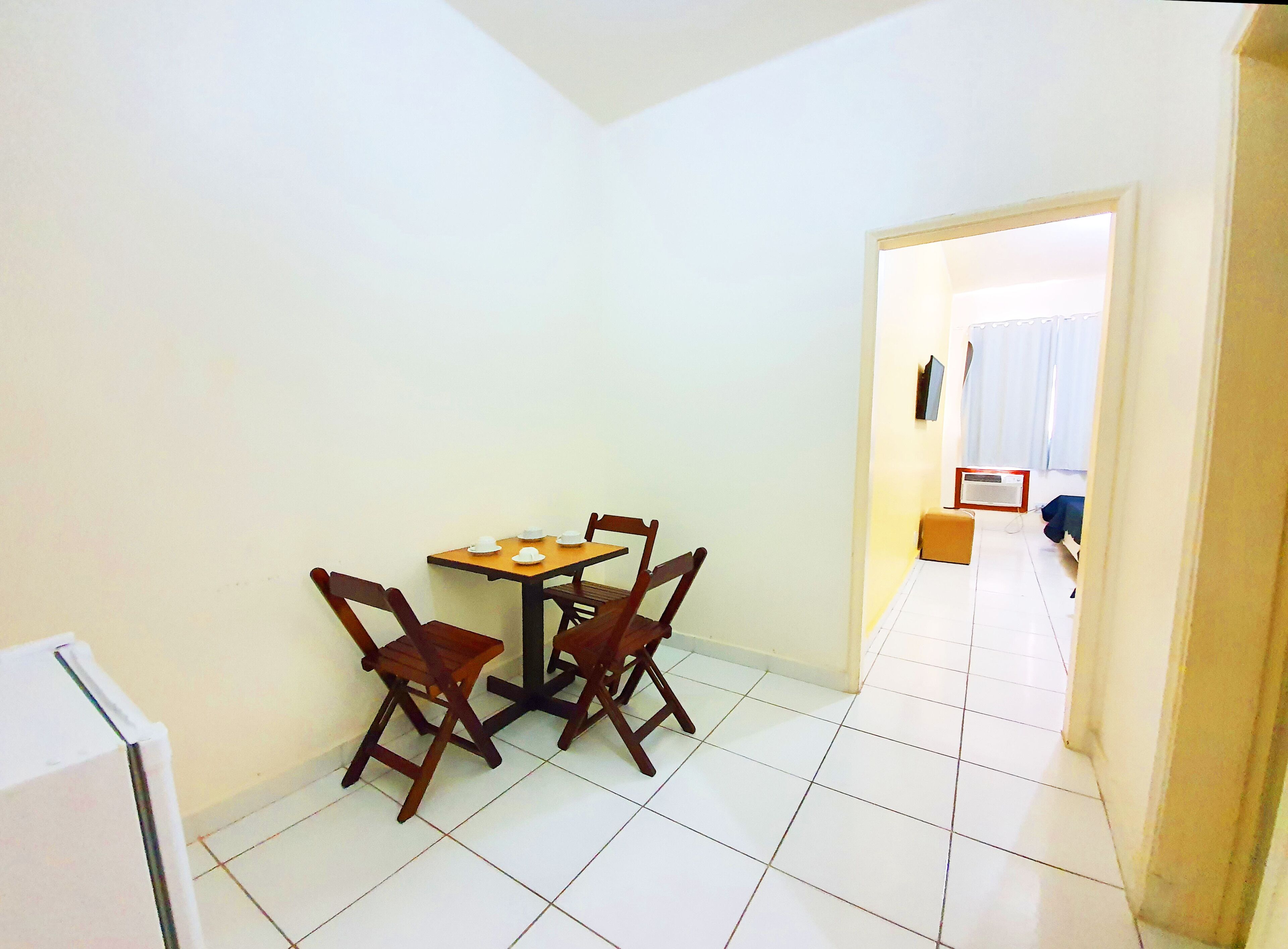 Een kleine, schone kamer met een betegelde vloer, een houten tafel met stoelen en een witte muur.