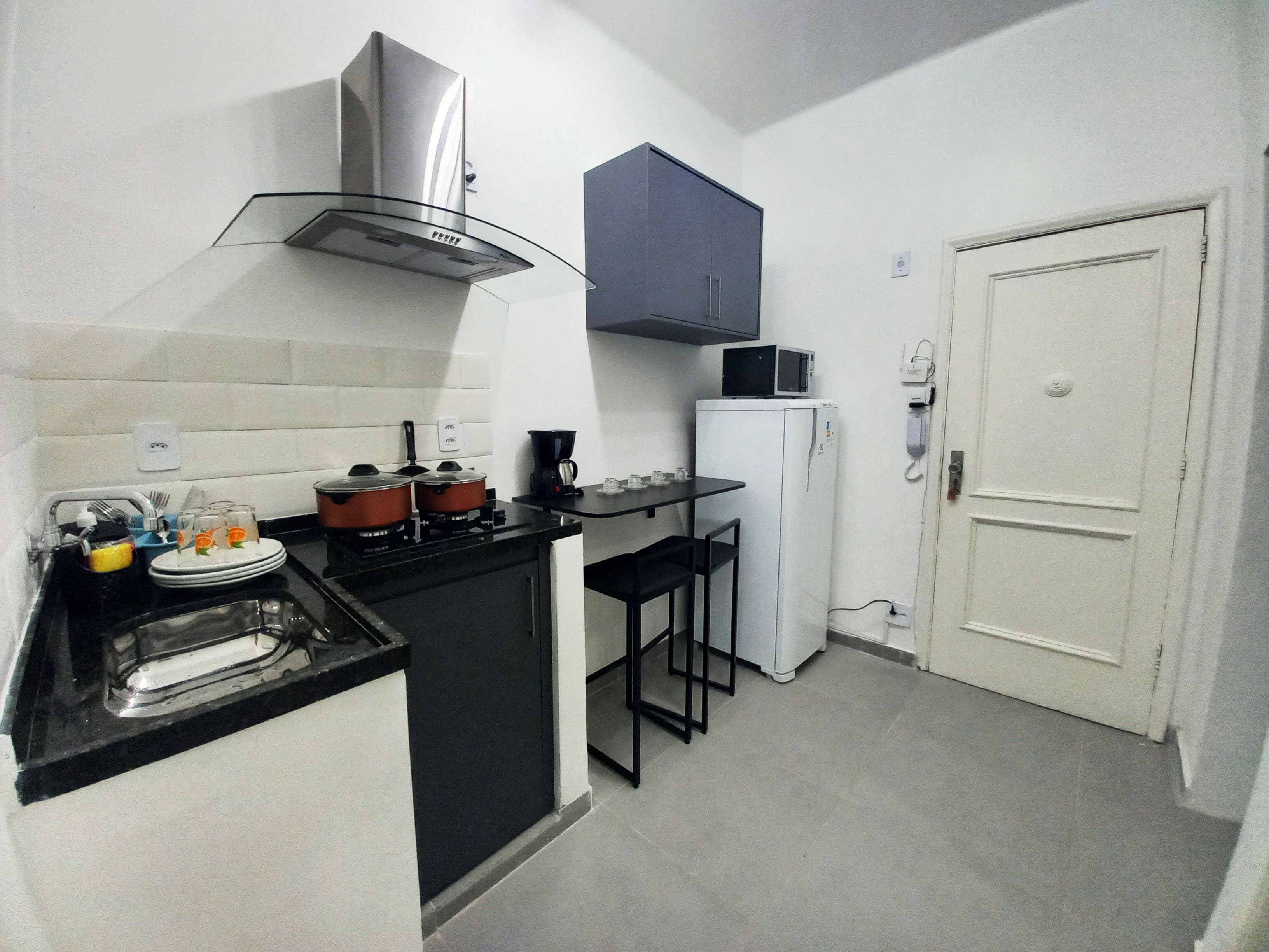 A compact kitchen with a gas stove, a microwave, a refrigerator, and a small bar stool.
