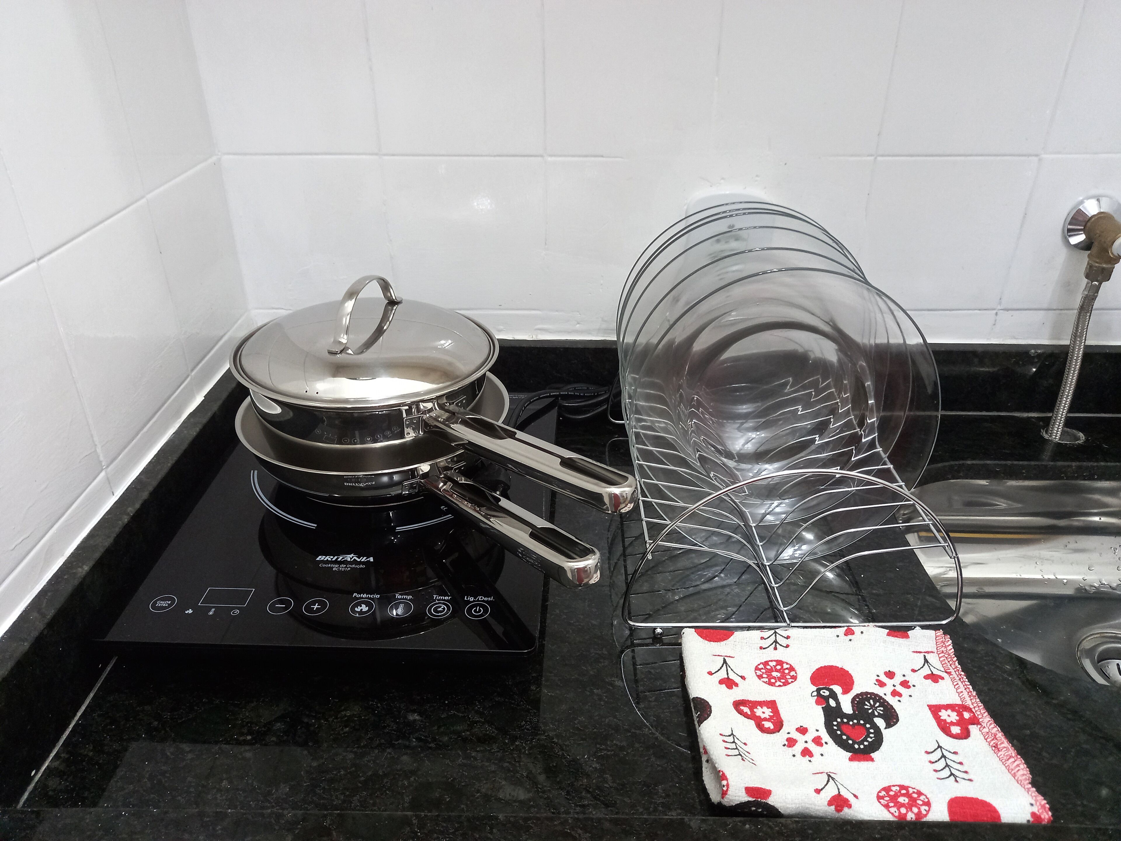 Une cuisine avec une plaque de cuisson à induction noire, une casserole dessus et un égouttoir à vaisselle en verre avec un torchon en dessous.