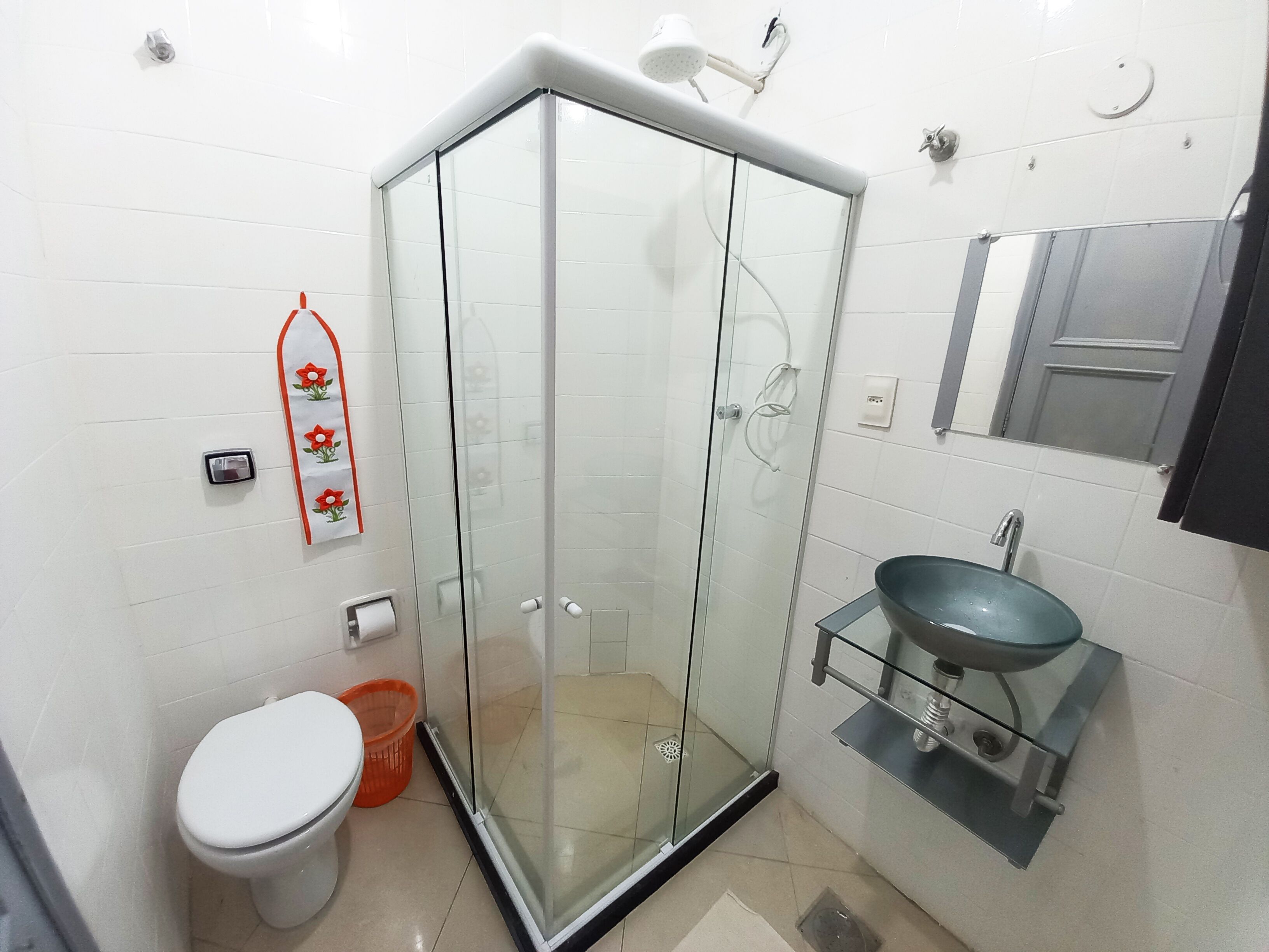 Un baño moderno con ducha envuelta en vidrio, inodoro blanco, lavabo con plato negro y espejo sobre el lavabo.