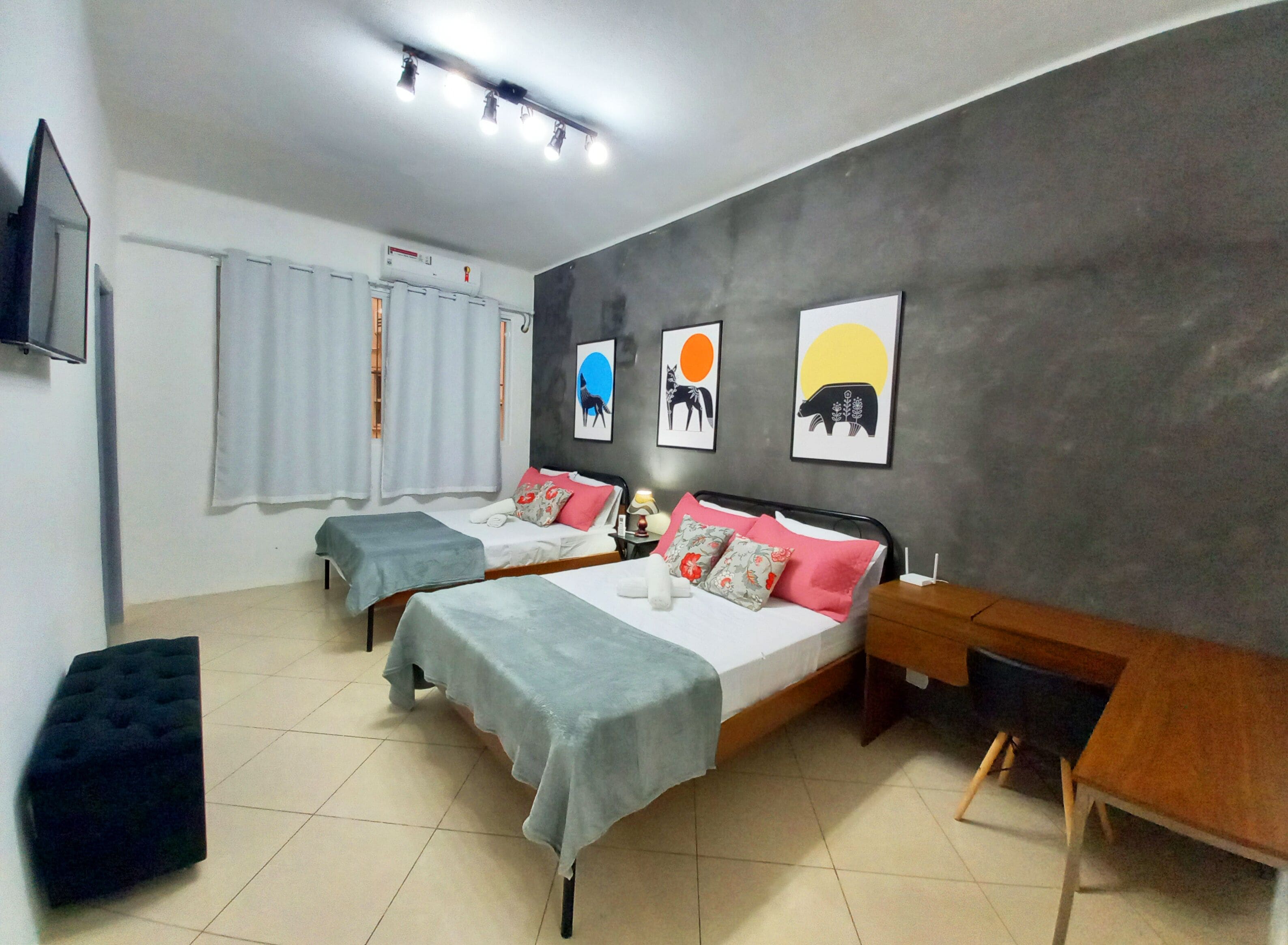 A hotel room with two beds, a TV, a window with curtains, and artwork on the wall.