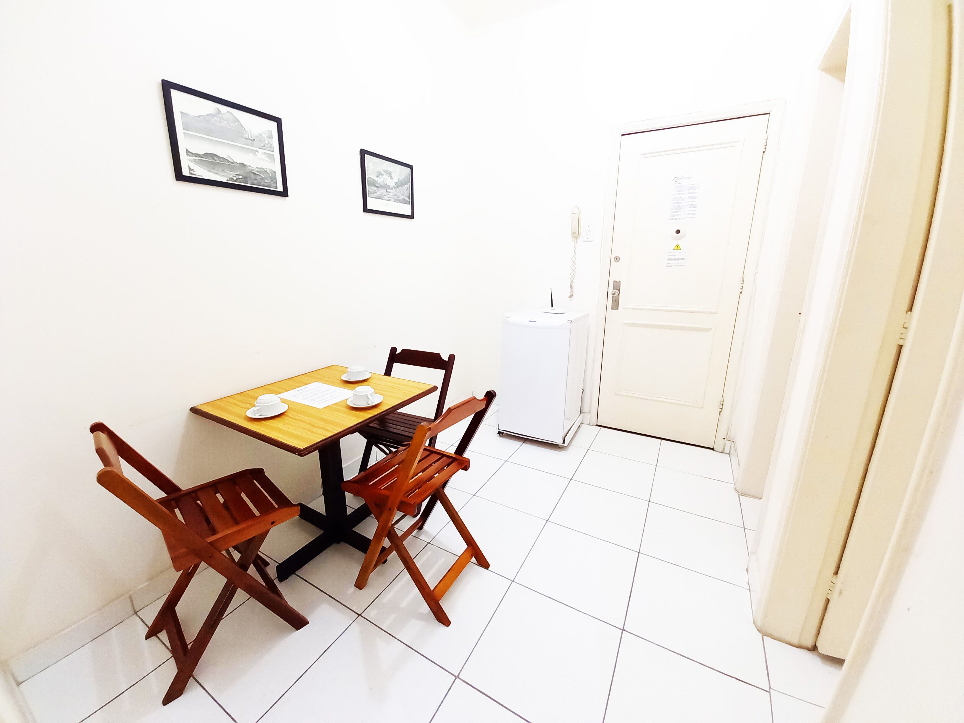 A small dining area with a wooden table and two chairs, a white door with a notice, and a white appliance.