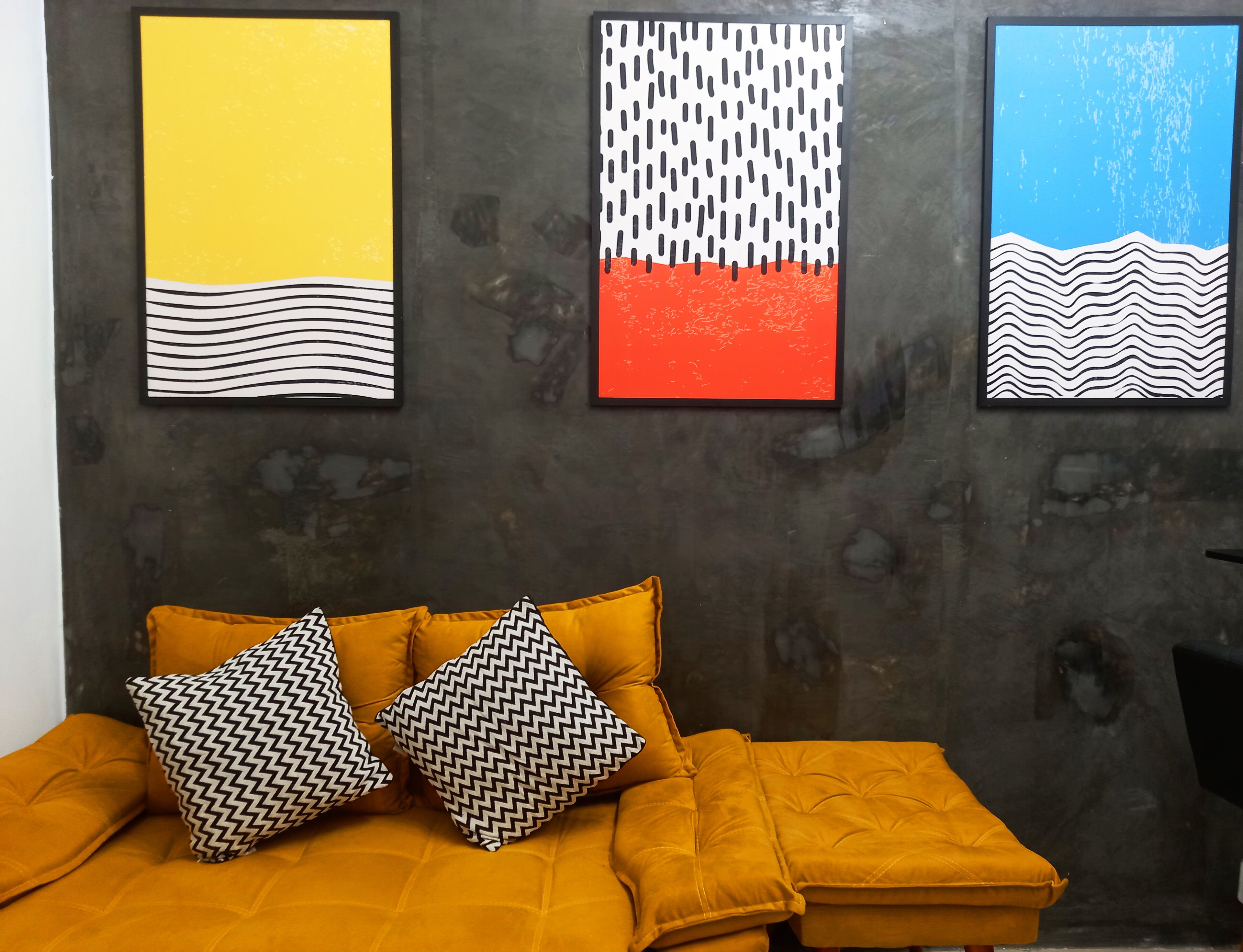 Een kamer met een bed, twee kussens met een patroon en drie abstracte kunstwerken aan de muur.