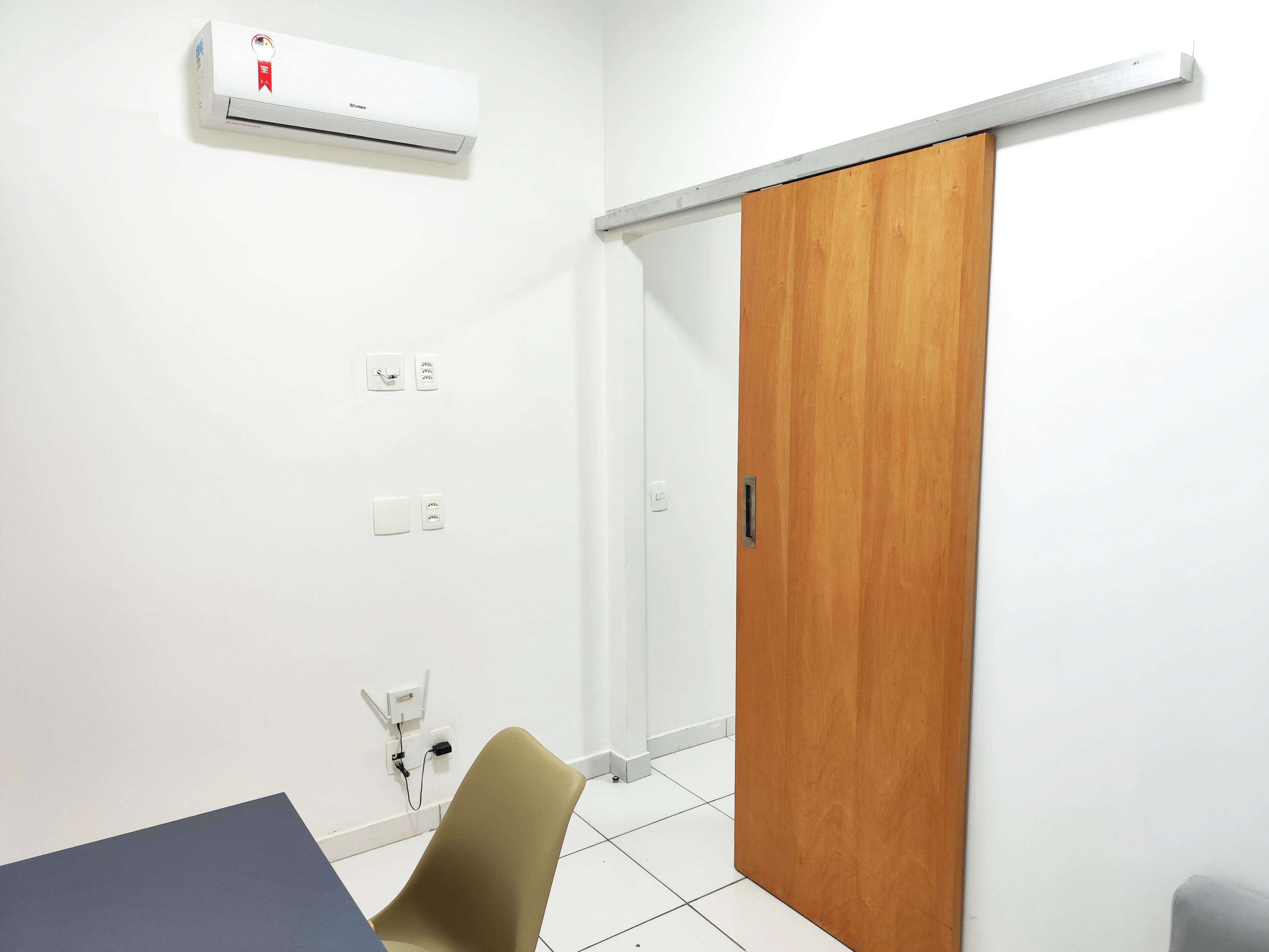Een kamer met een schuifhouten deur, een witte airconditioning en een bureau met stoel.