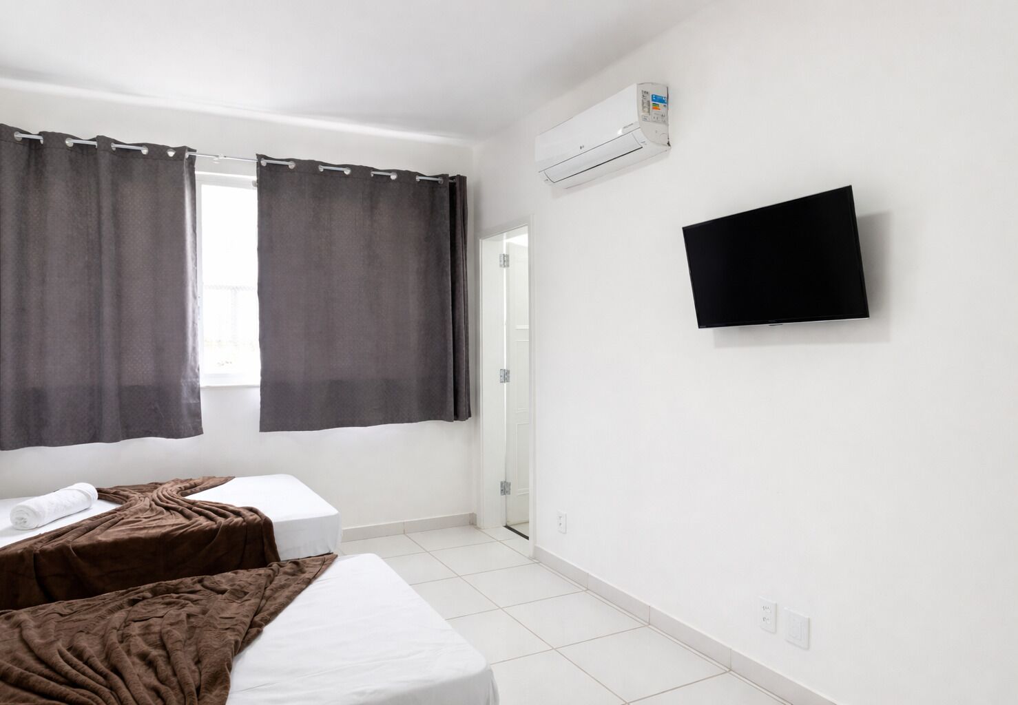 A hotel room with two beds, a flat-screen TV mounted on the wall, and an air conditioning unit above the door.