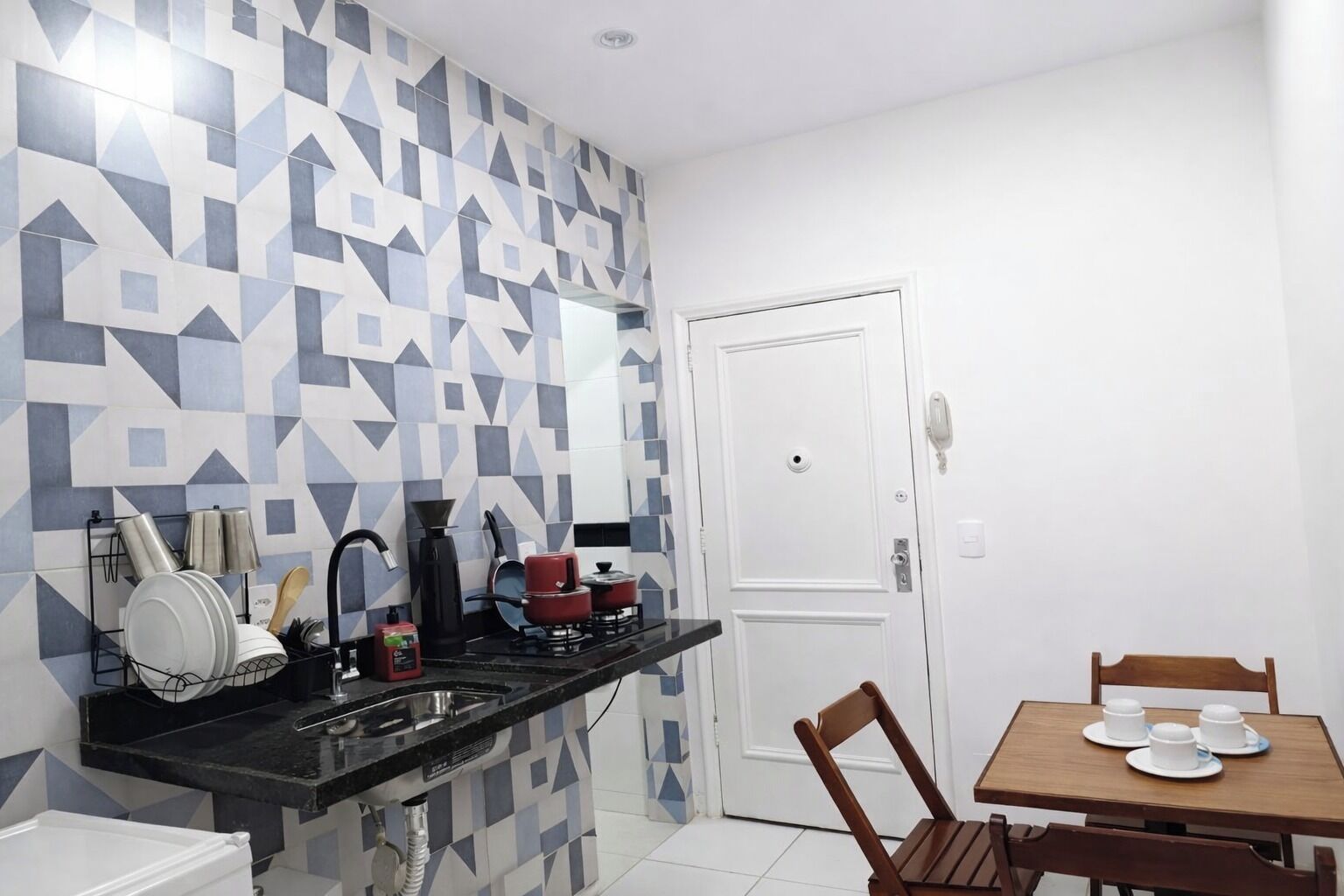 A compact kitchen with a black countertop, a stove, and a sink. There is a dining area with a wooden table and chairs.