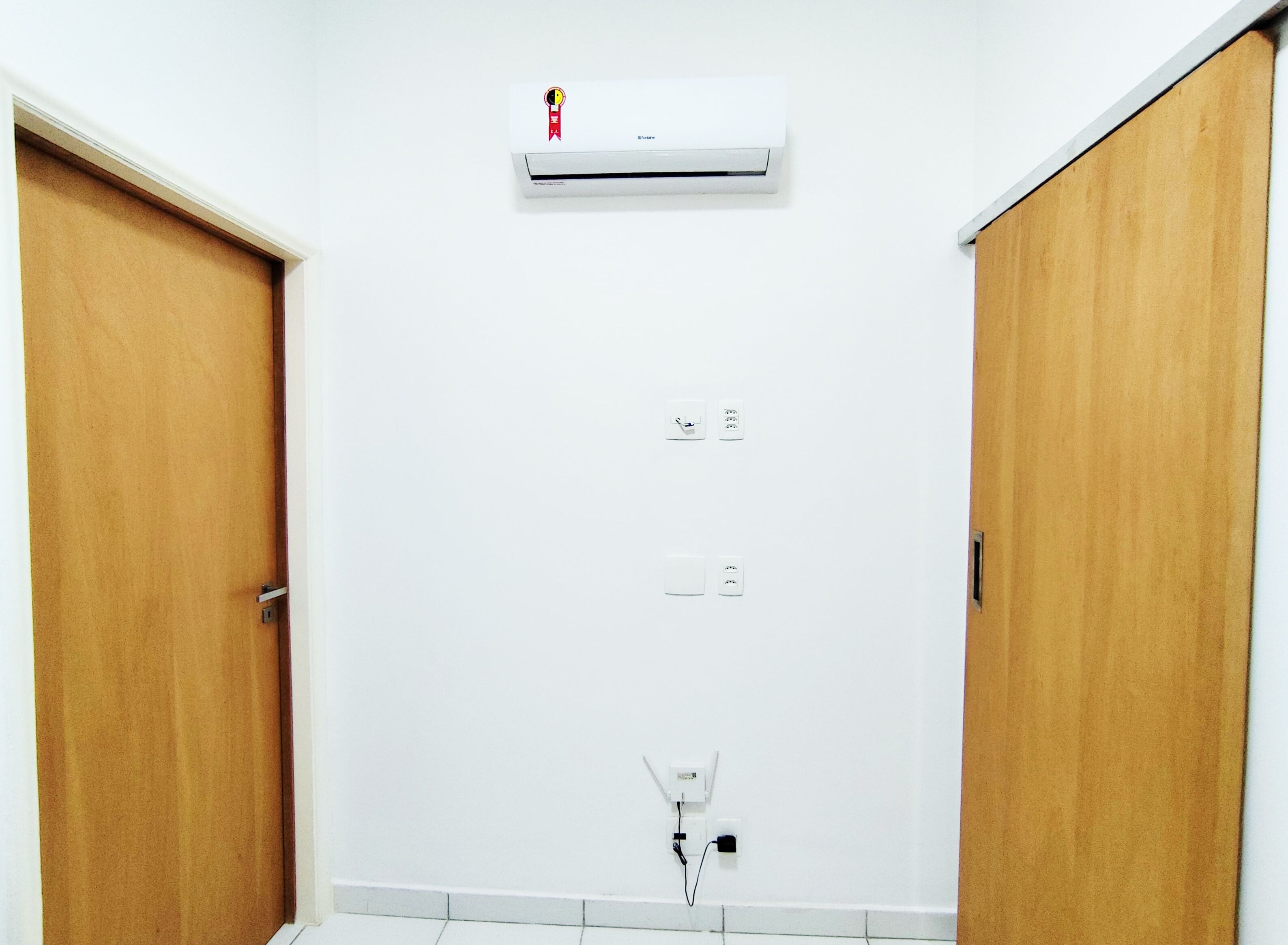 A room with a white wall, a ceiling-mounted air conditioner, and two wooden doors.