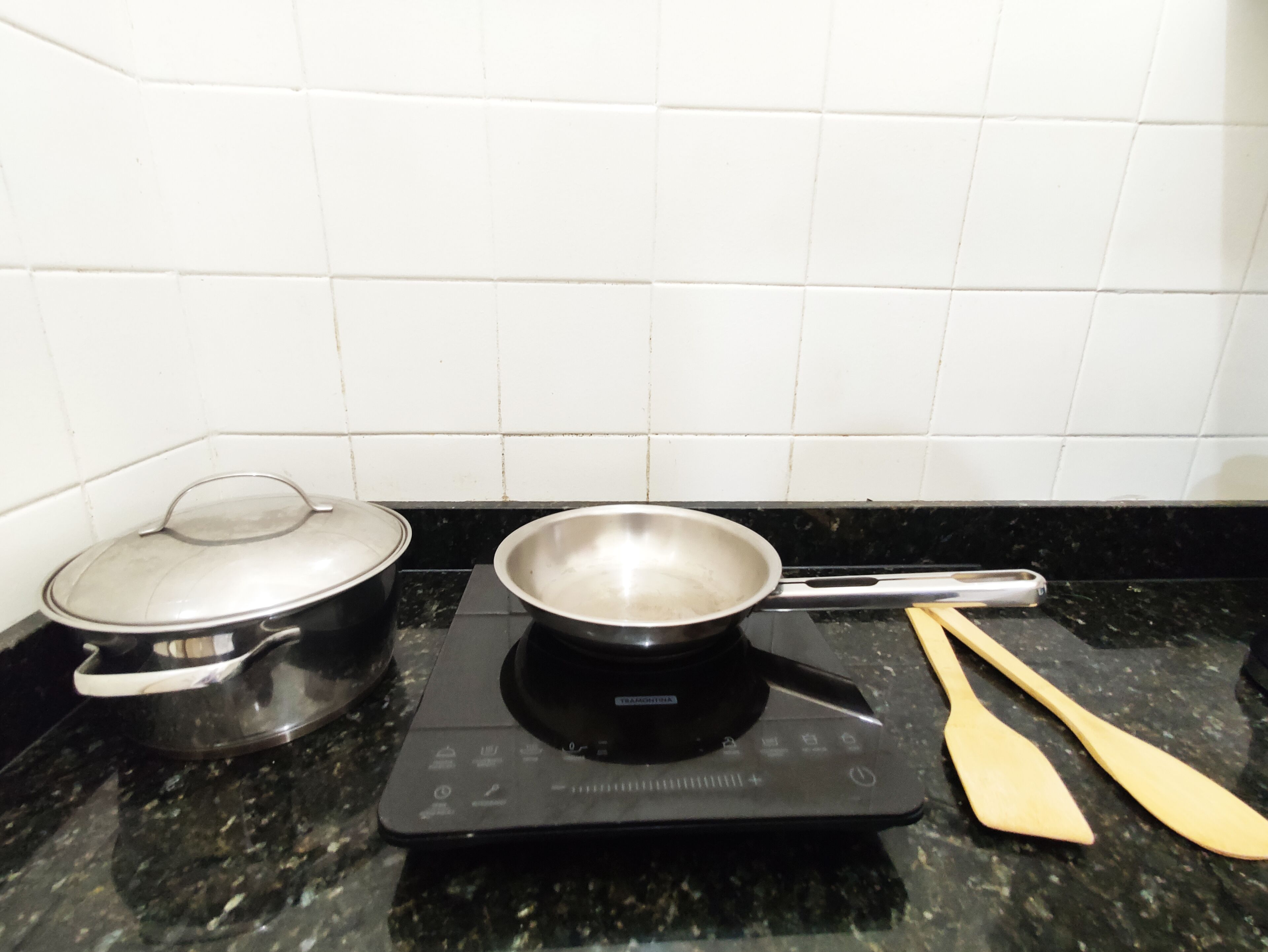 A kitchen with a stove, a pot, and wooden utensils on a granite countertop.