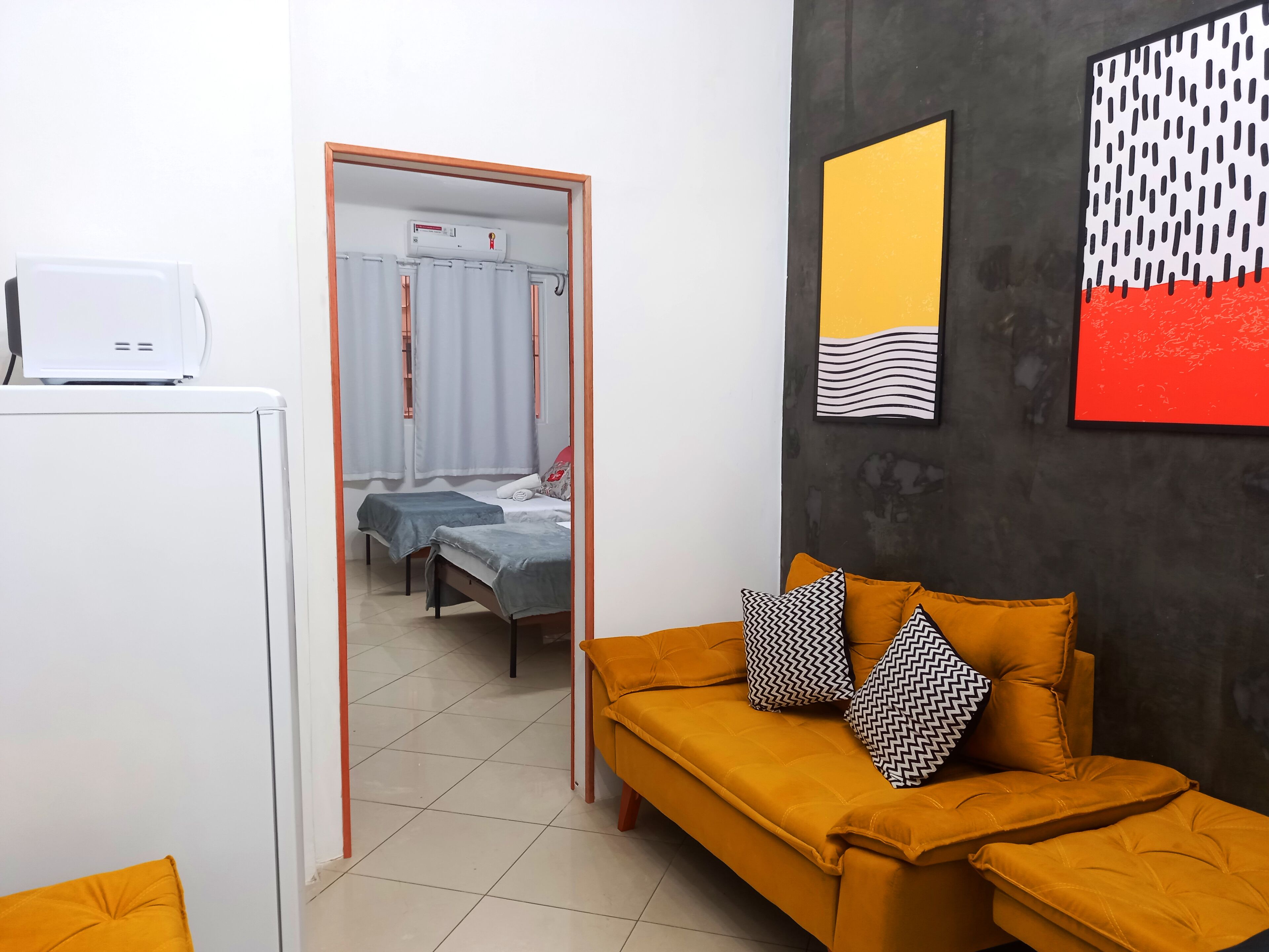 A room with a sofa, a bed, a small table, and a wall with abstract art.