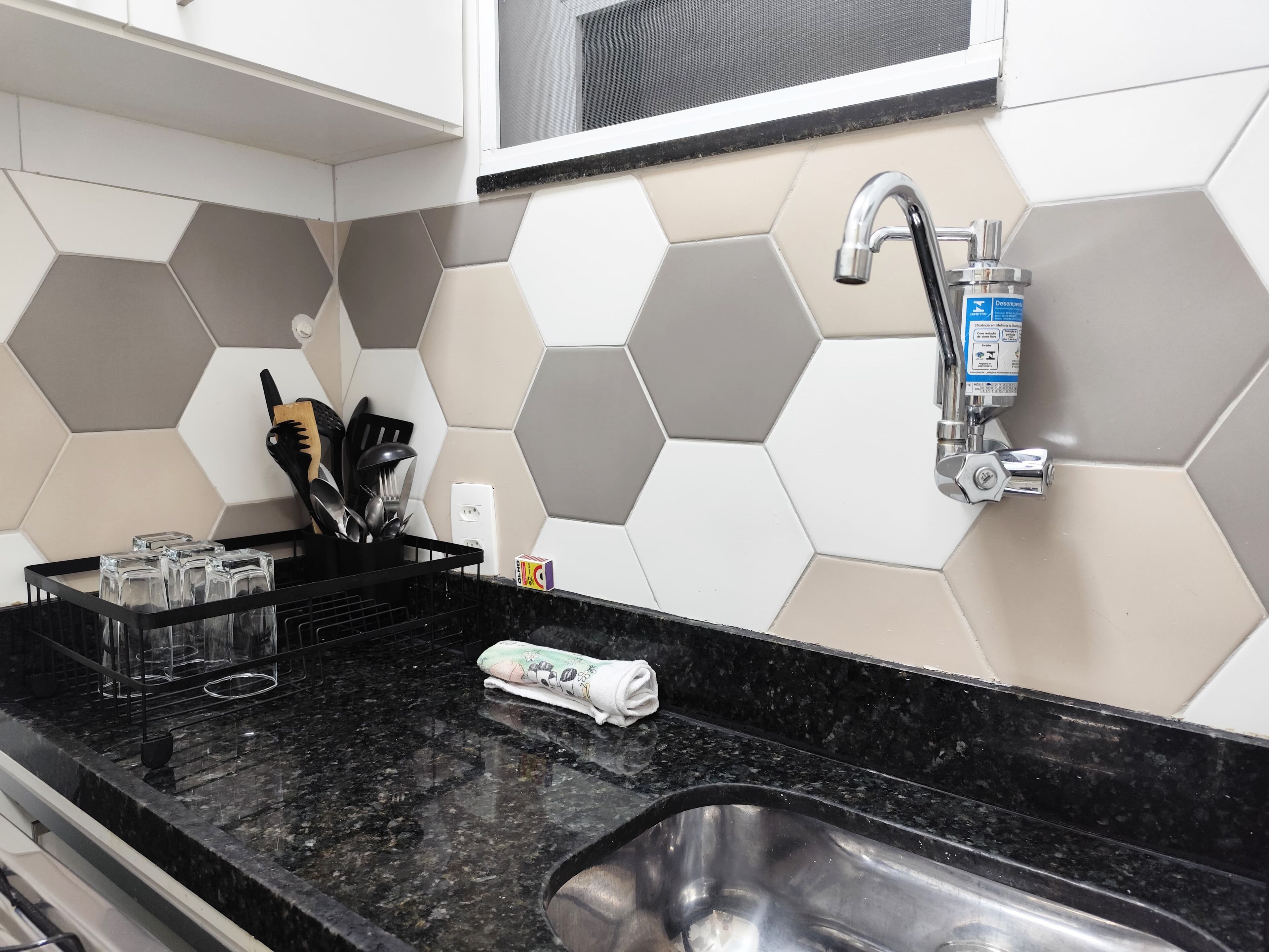 Una cocina con encimera de granito negro, un lavamanos de acero inoxidable y una ventana sobre el lavamanos.