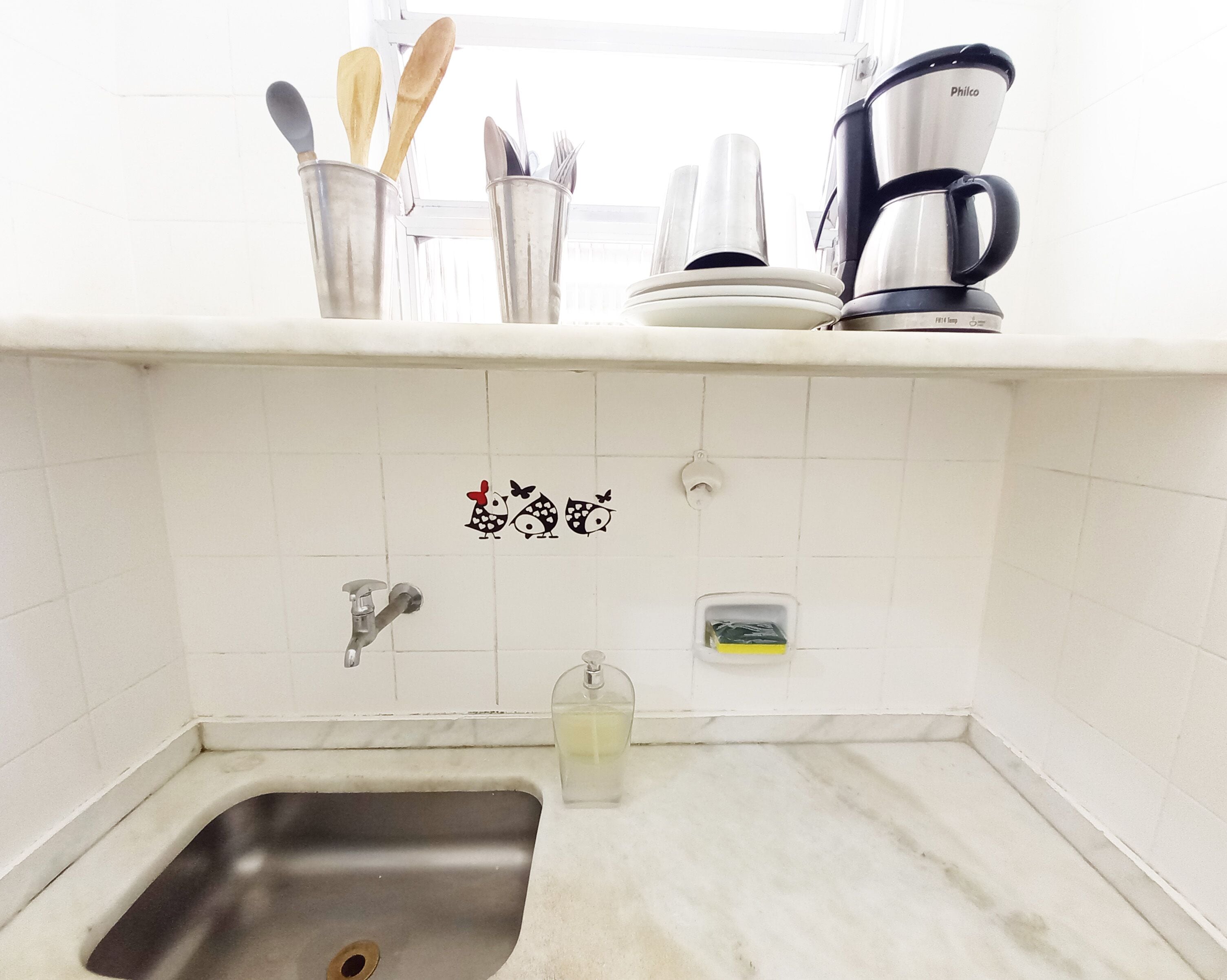 A kitchen with a stainless steel sink, a coffee maker, and utensils in a metal container.